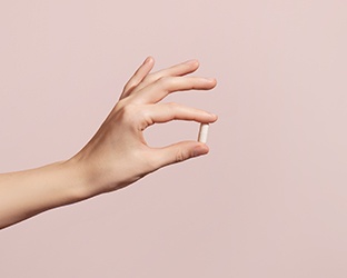 Person’s hand holding pill against neutral background