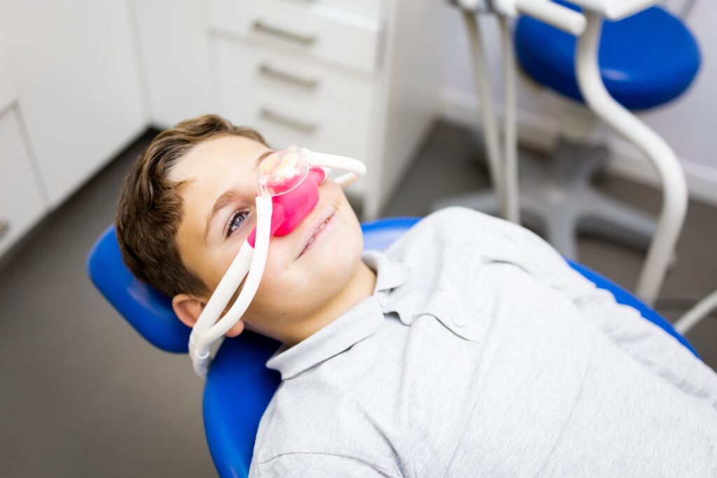 Little boy in dental chair with pink nitrous oxide mask over nose